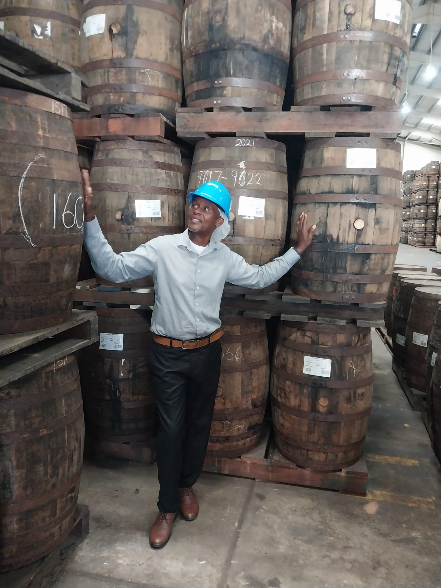 Anthony Clarke, owner of On The House Taxi Service, smiling beside rum barrels during a Barbados rum tour