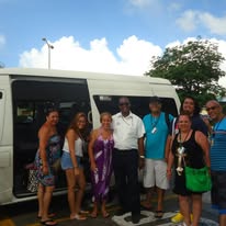 Happy guests standing beside the On The House Taxi Service van after group transportation in Barbados