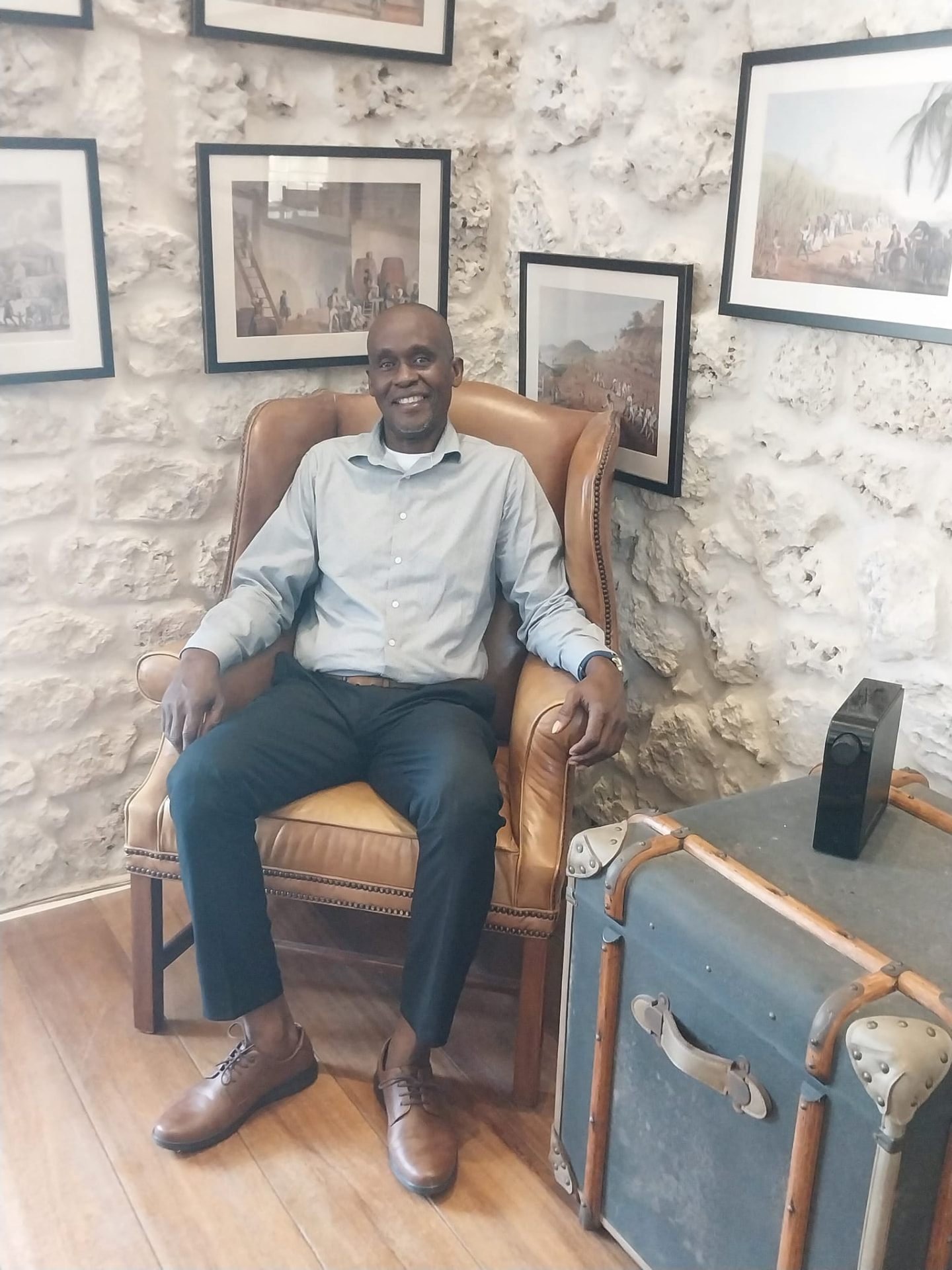 Anthony Clarke, owner of On The House Taxi Service Barbados, seated and smiling in a historic Barbadian coral stone building