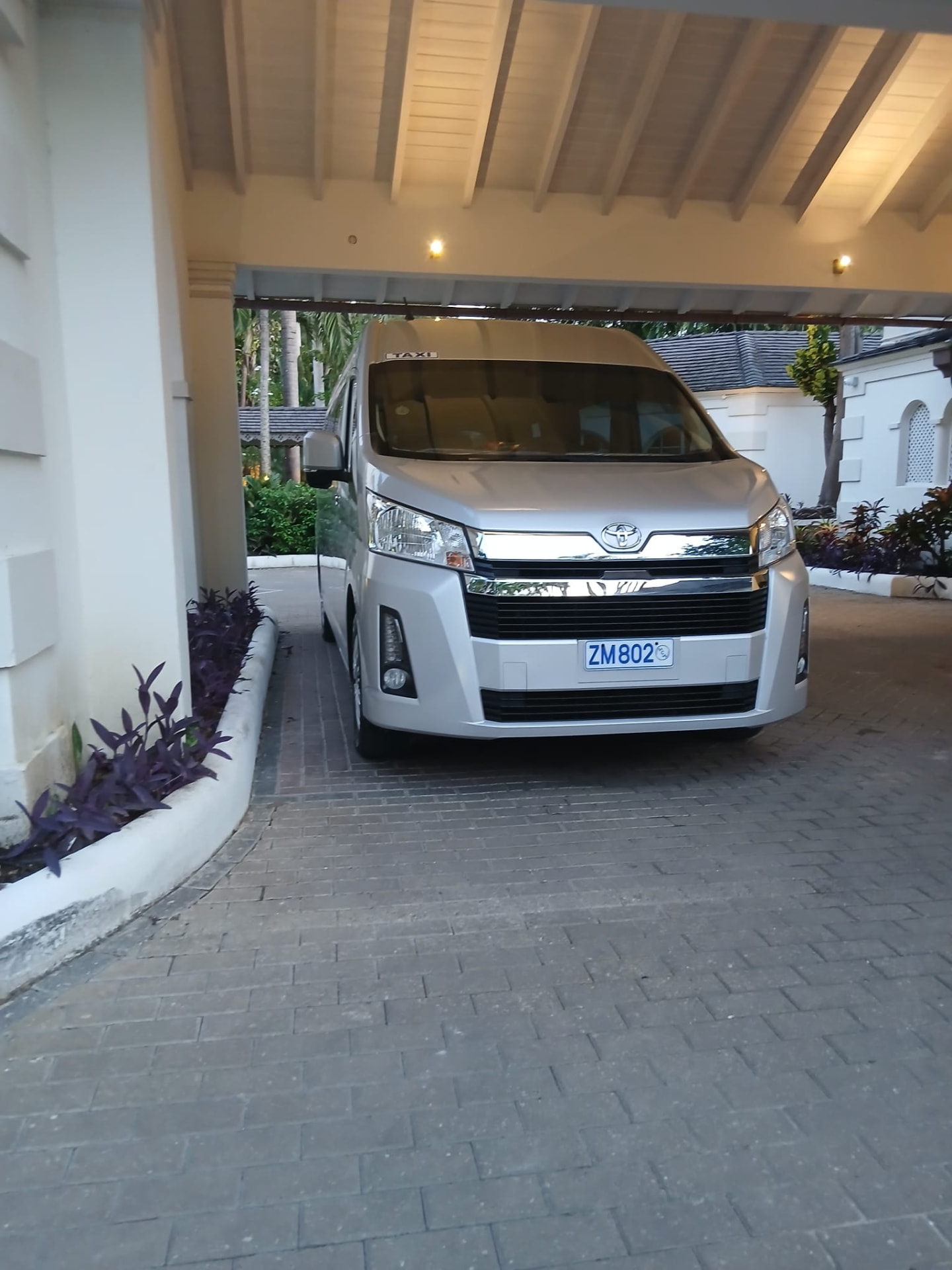Silver 13-passenger Toyota Hi Ace luxury van from On The House Taxi Service parked under a hotel porte-cochère in Barbados