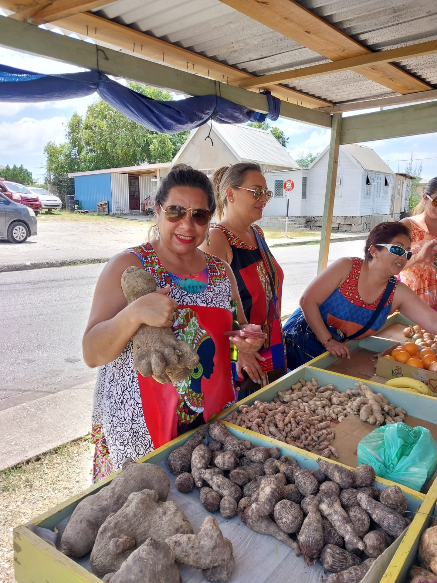 Guests choosing fresh local vegetables at a Barbados market stall on a shopping trip with On The House Taxi Service