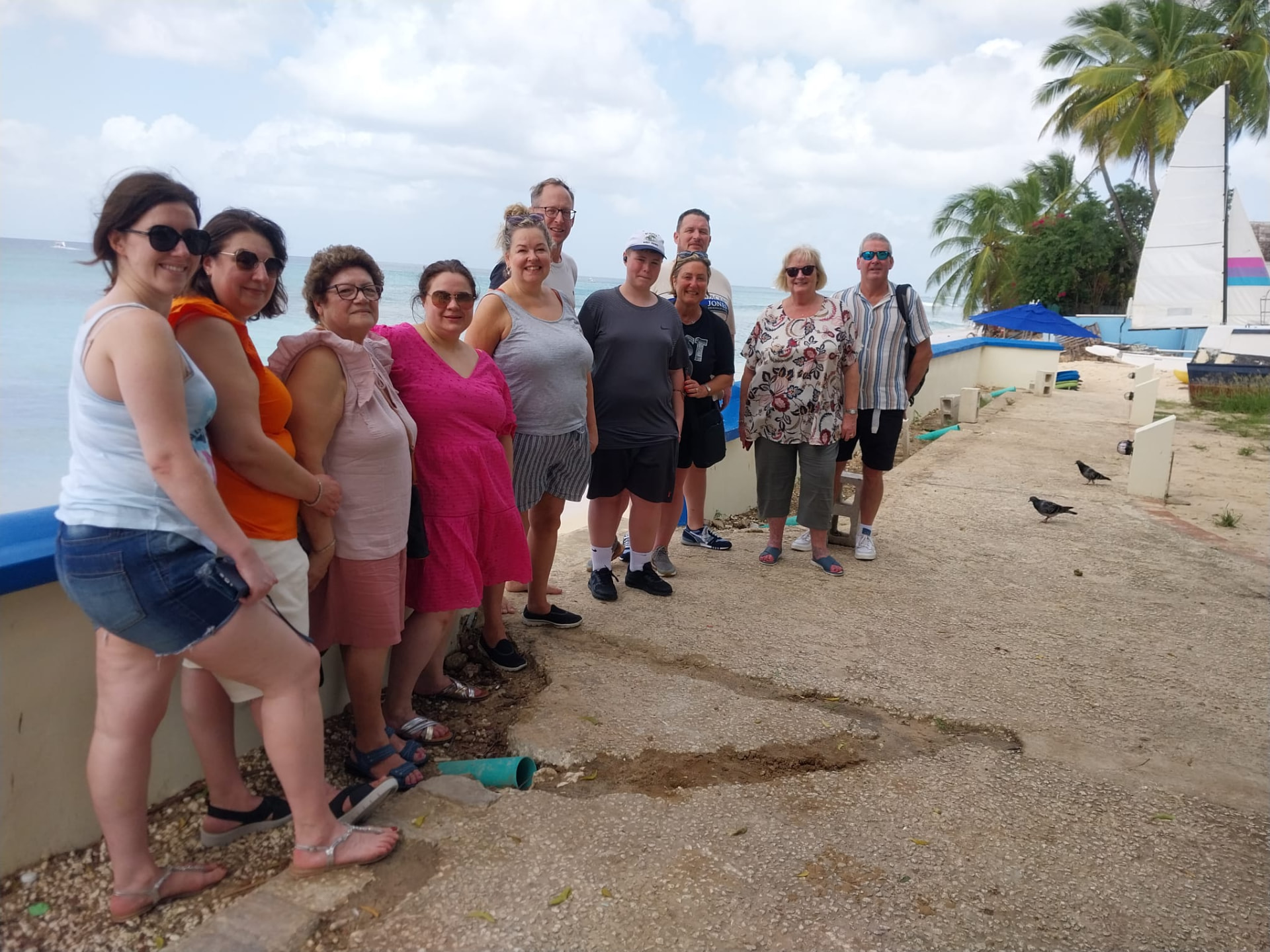 Tour group beside a white sailboat at a Barbados beach stop in bright daylight